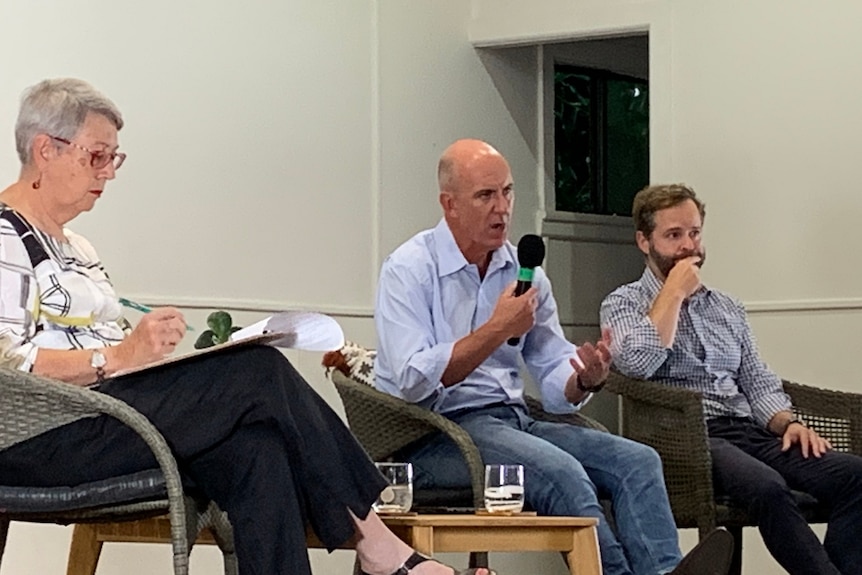 A woman and two men, one of whom is speaking into a microphone, on stage at a community event.