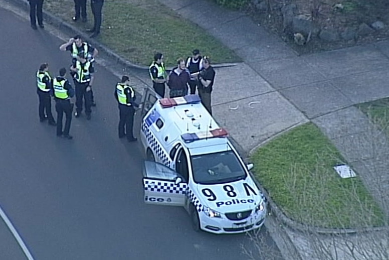 Police officers escort a man to a police divvy van outside a house.