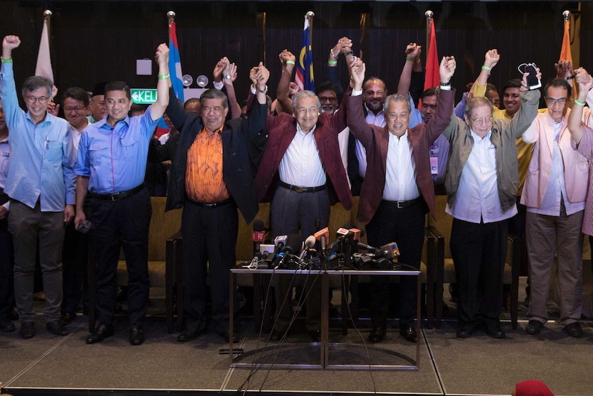 Mr Mahathir and other coalition leaders hold hands and raise them in the air standing side by side.