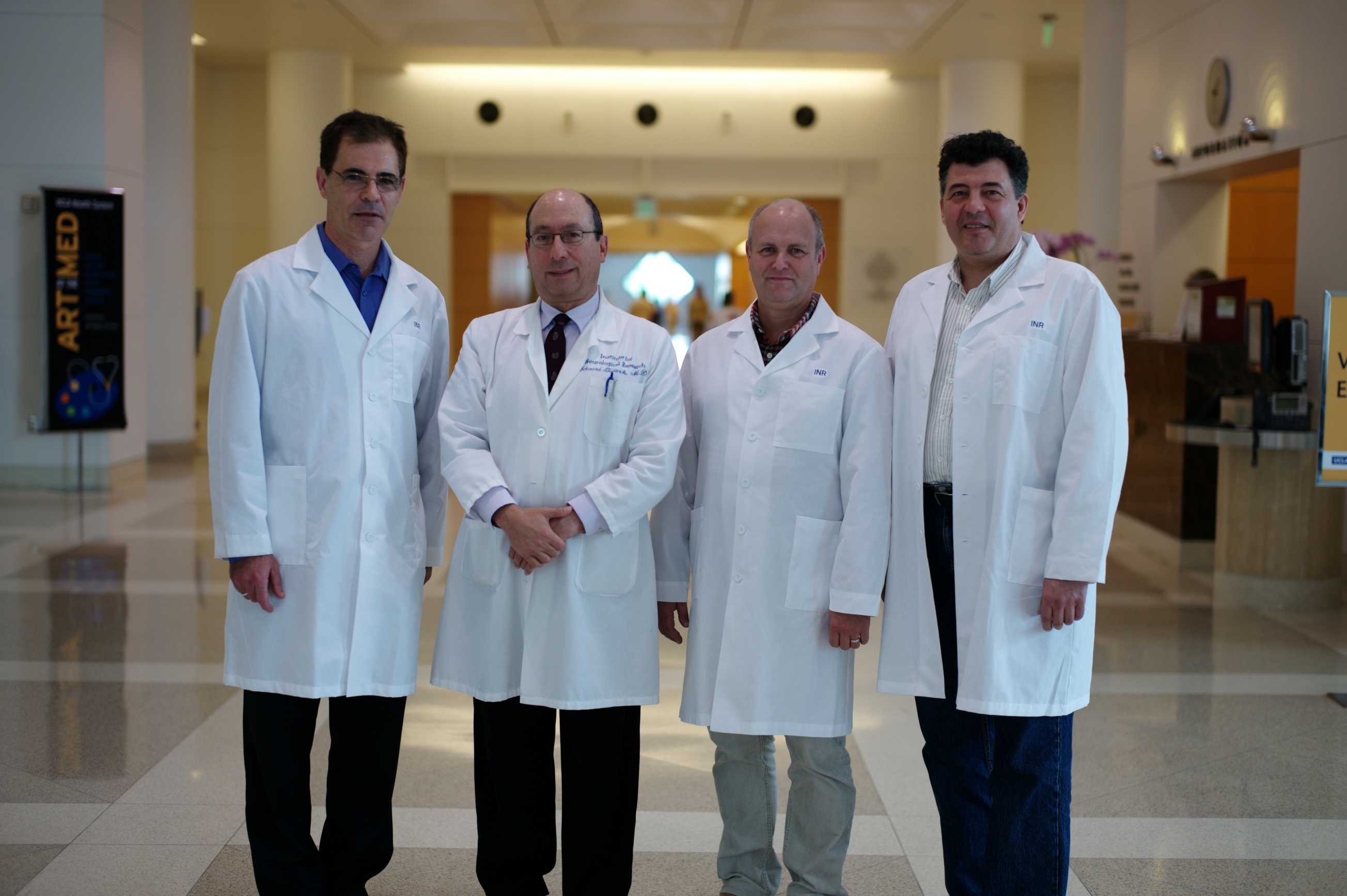 Four medical professionals in white coats stand together at conference.