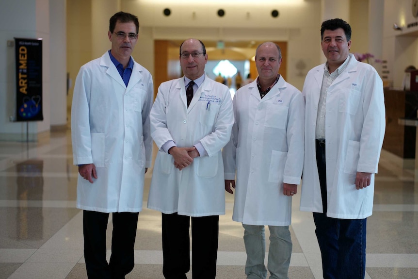 Four medical professionals in white coats stand together at conference.