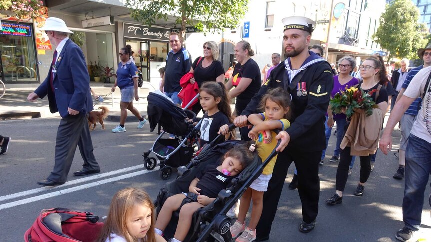 A group of people walk down a street in Redfern, kids in strollers.