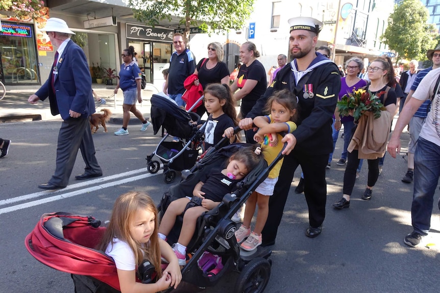 A group of people walk down a street in Redfern, kids in strollers.