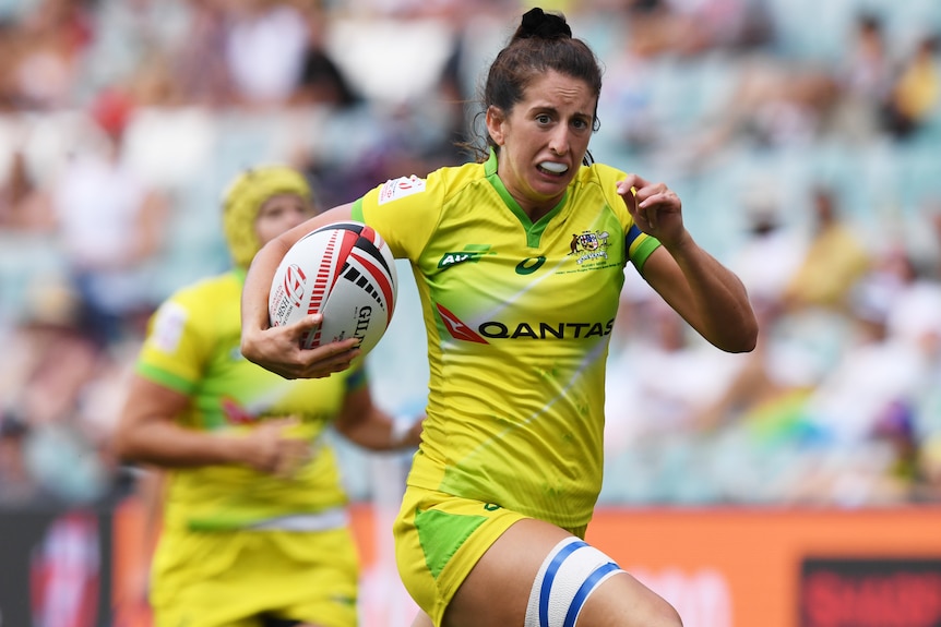 Woman running with the ball tucked under her arm during an rugby sevens match