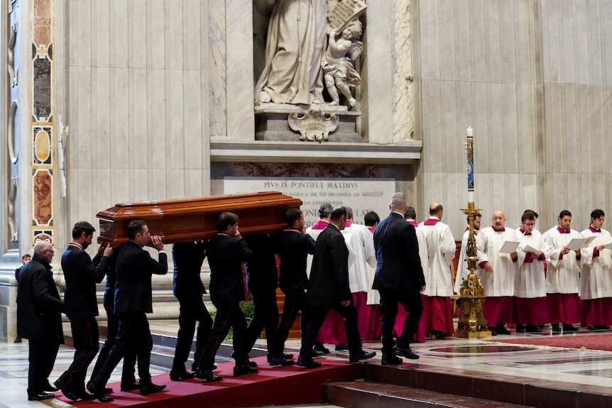 Pallbeares carry a coffin of Cardinal George Pell.