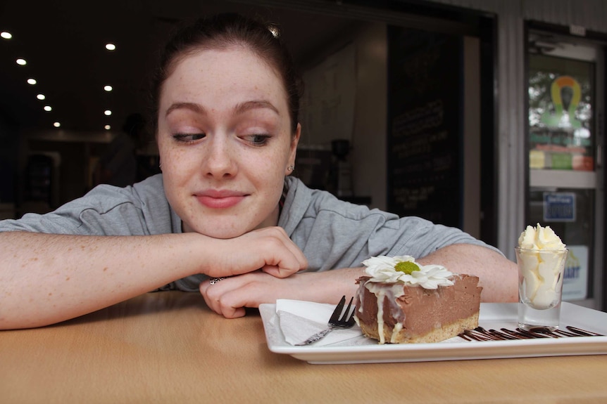 Phoebe Clarke leans on a table and looks at a piece of cake.