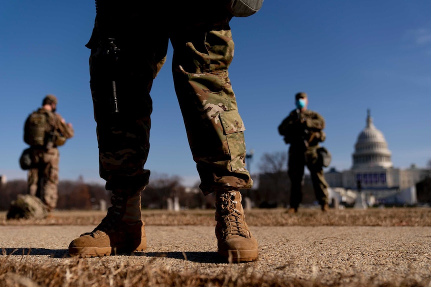 The legs of a person in military clothing in focus, with the US Capitol Building in the background.
