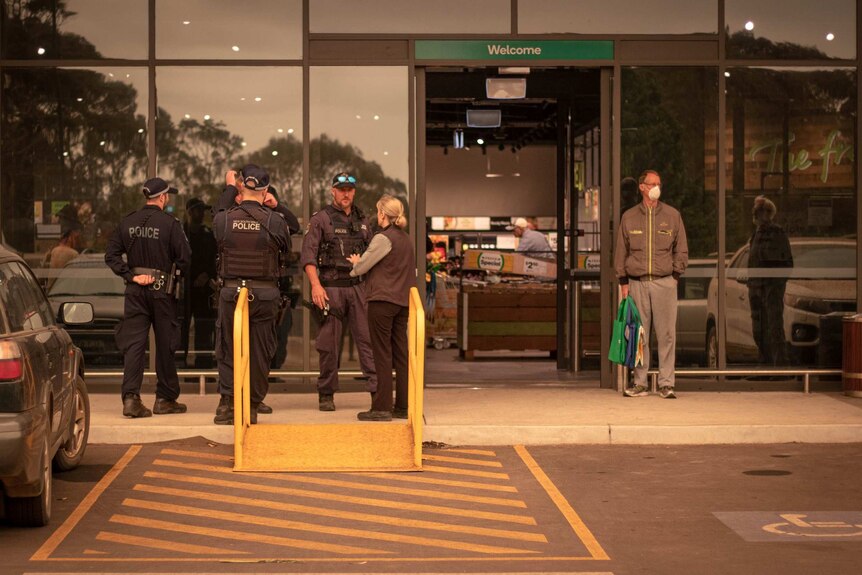Four police officers stand next to the entrance to a Woolworths supermarket at Narooma.