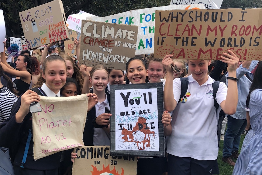 A group of young female students in school uniform hold signs calling for action on climate change.