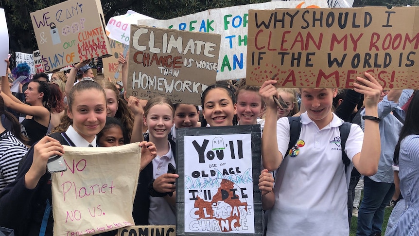 A group of young female students in school uniform hold signs calling for action on climate change.