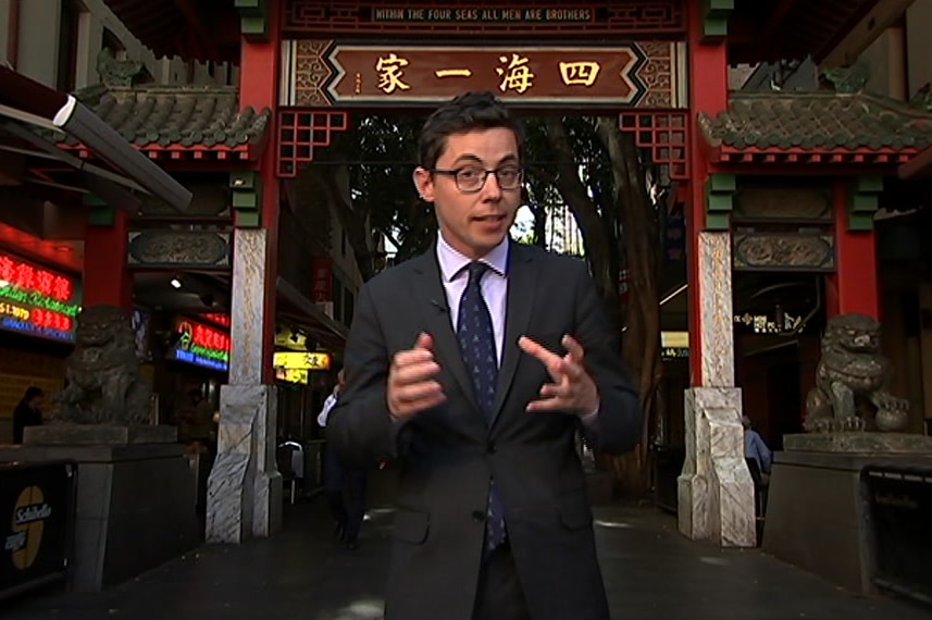 Dziedzic talking to camera with Chinese signage and arch in background.