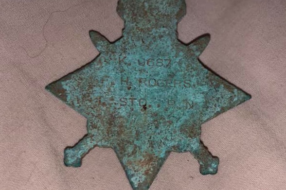 The back of a war medal with green patches and a faint engraving showing a name, rank and service number.