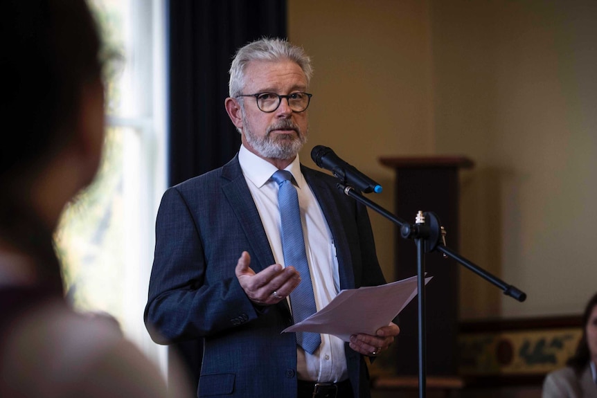 Man wearing a suit stands at a microphone