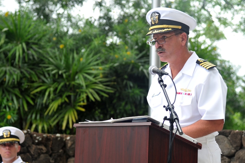 Naval officer stands at a lectern and speaks. 