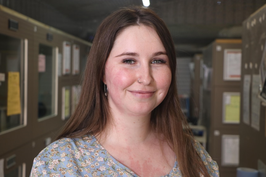 A woman with brown hair poses for a photo in a corridor.