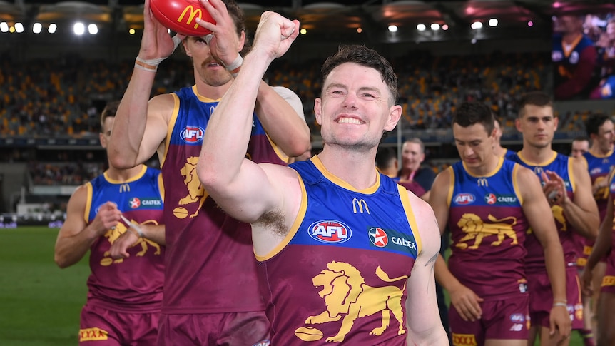 Lachie Neale smiles and pumps his fist towards the crowd as he leads the Lions off the Gabba