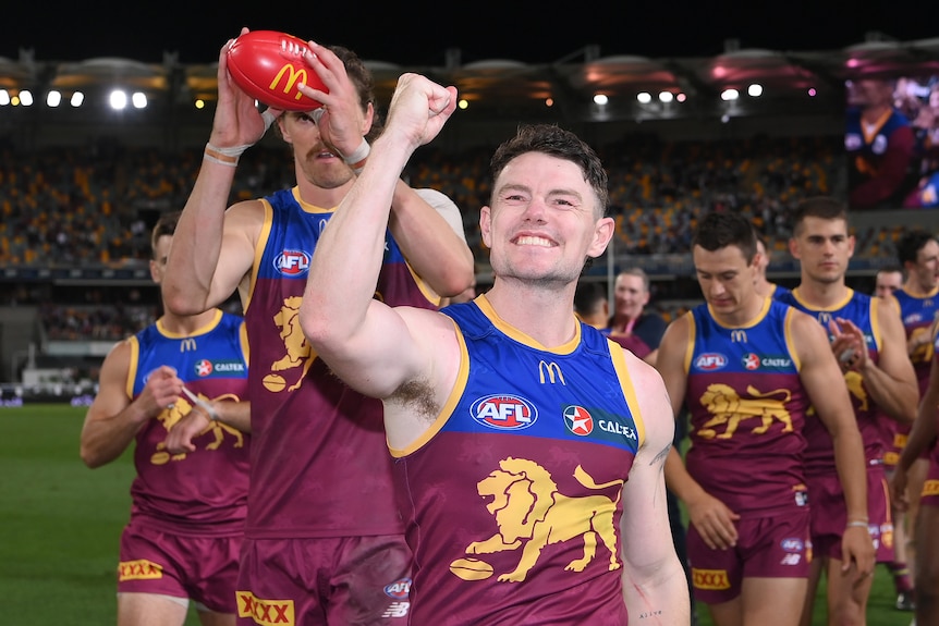 Lachie Neale smiles and pumps his fist towards the crowd as he leads the Lions off the Gabba