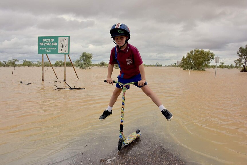 Ethan Cox jumps holding his scooter in floodwaters at the Western River on the edge of Winton.