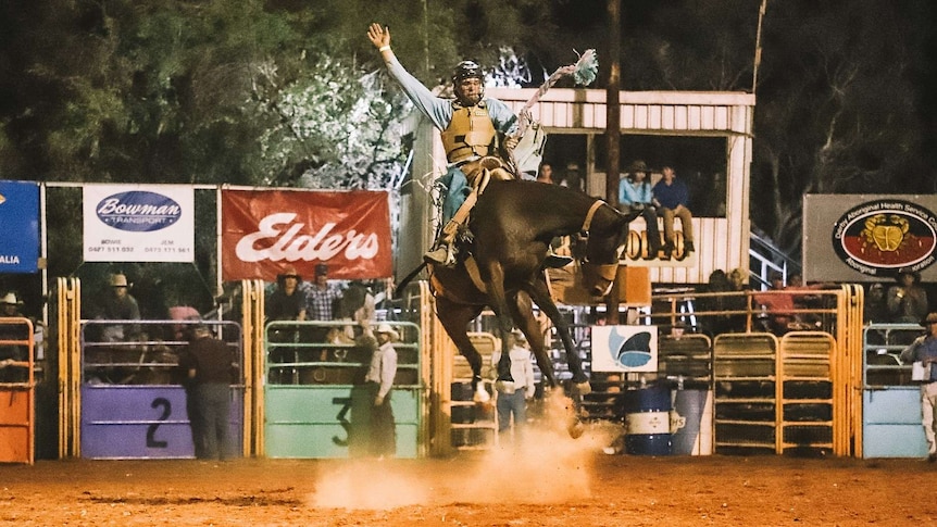 A horse bucks a man with a helmet into the air