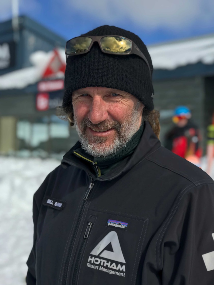 A man with a black beanie and sunglasses standing in the snow.