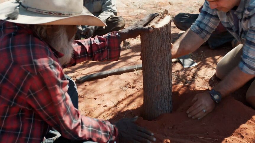 Phil Breslin and Indigenous men chop a piece of wood