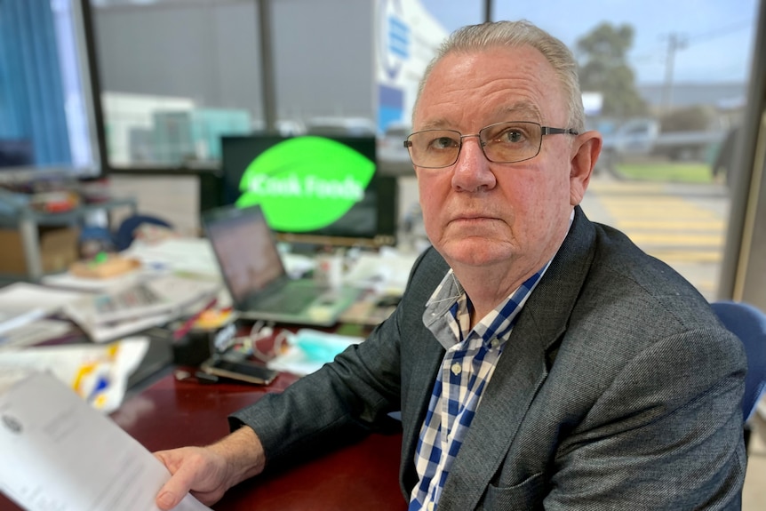 Ian Cook wearing a suit, sitting at a desk and holding paper documents.