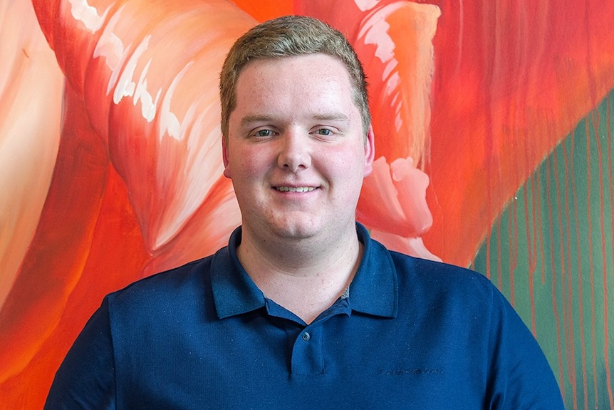 Mitchell Sprague stands in front of a colouful wall.