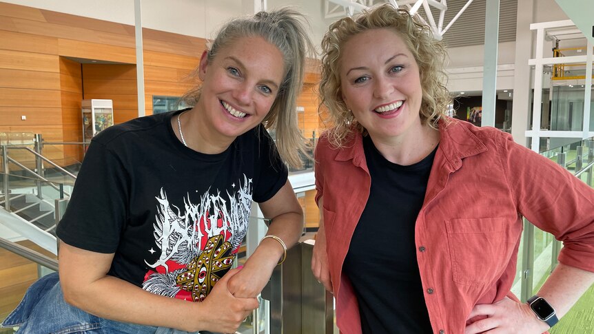 Catherine and Zan smile at the ABC in Melbourne. Catherine wears a black band t-shirt and Zan wears a red long sleeve shirt