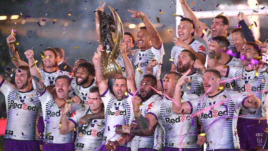 Melbourne Storm players point their fingers and lift a trophy