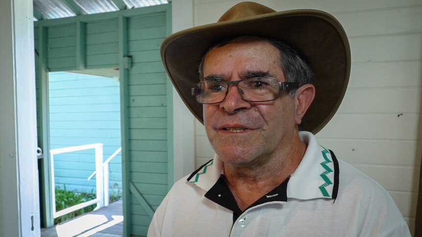 Older Aboriginal man in cowboy hat standing in old school building