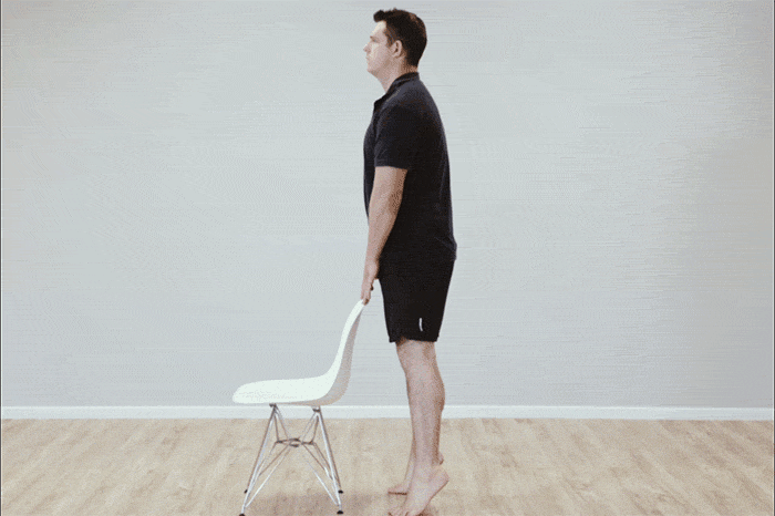 A man standing with a chair demonstrating heel raise exercises to strengthen his muscles for standing up for long periods.