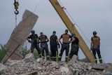 Six rescue workers in protective gear stand atop the wreckage of a residential building.