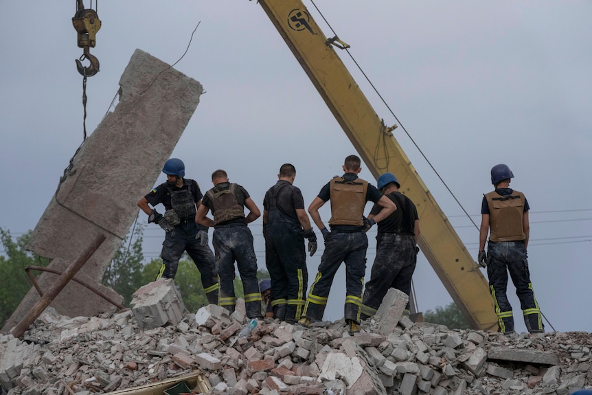 Six rescuers in protective gear stand atop the wreckage of a residential building.