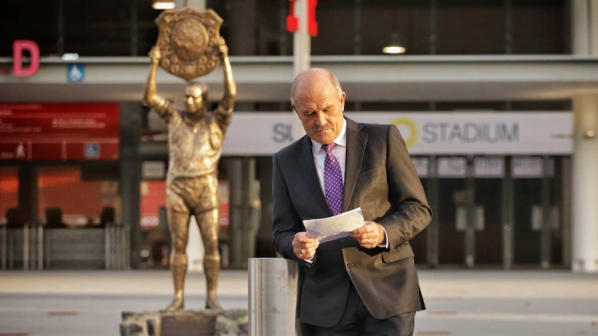 A man leans on a pole reading a piece of paper.
