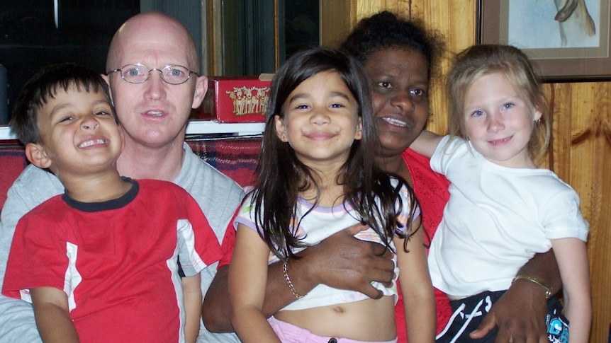 A man and woman sit on a couch with three children sitting in their laps.