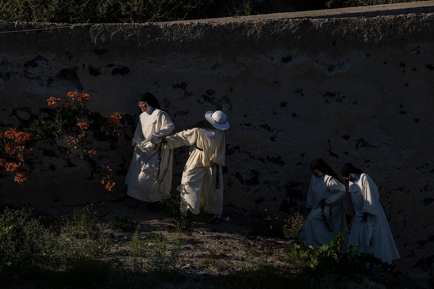 Las monjas caminan por el jardín de la iglesia y se ayudan mutuamente a subir la colina. 