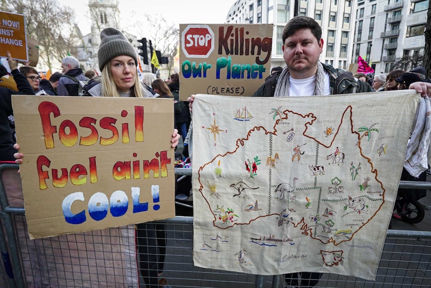 a woman and man holding up signs while protesting against climate change inaction
