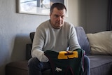 A man holding a Tasmanian football jersey looks up at the camera.