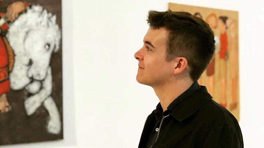 A man looking up and smiling in front of two framed art pieces