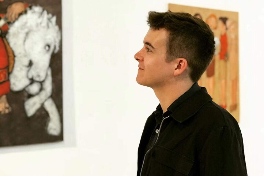 A man looking up and smiling in front of two framed art pieces