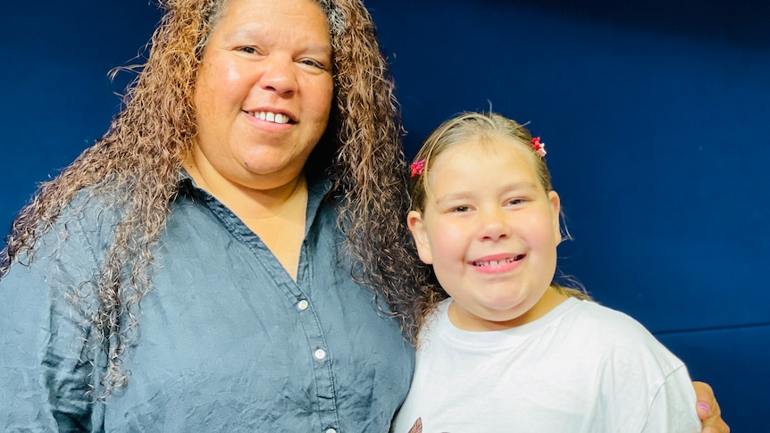 woman with long curly hair standing with her arm around her daughter, both smiling