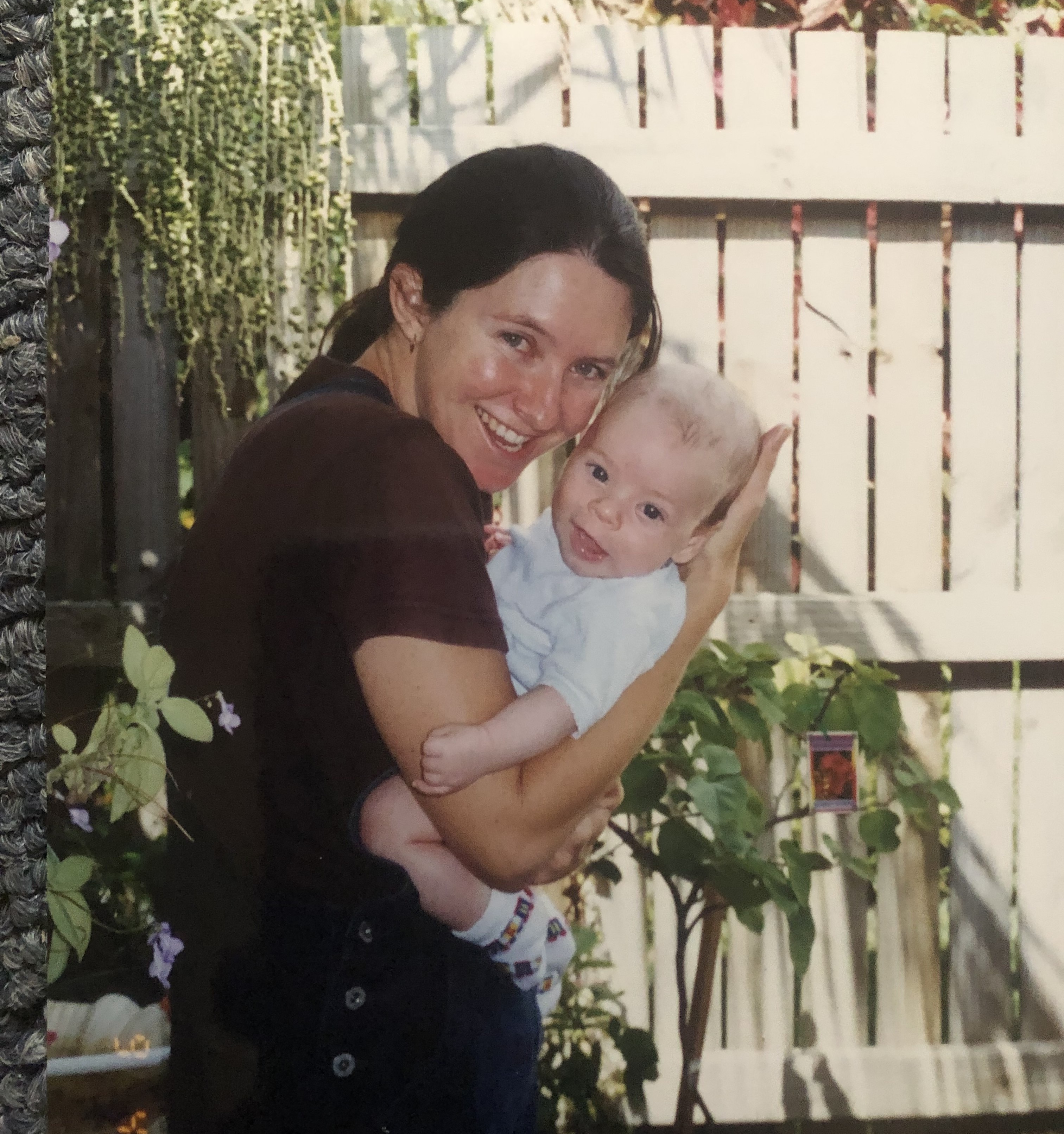 Una mujer sostiene a un bebé en un patio trasero, ambos sonriendo a la cámara.