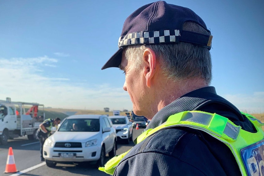 A Victoria Police officer stands at the side of the freeway at a police checkpoint.