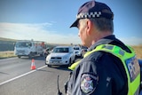 A Victoria Police officer stands at the side of the freeway at a police checkpoint.