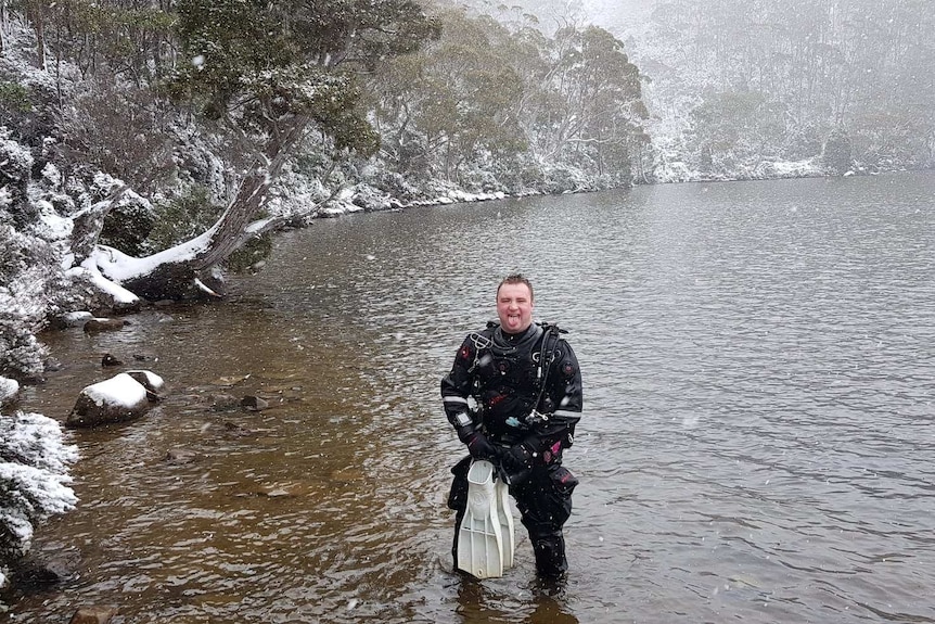 A member of the dive club stands in Lake Dobson. Snow covers the lake edge.