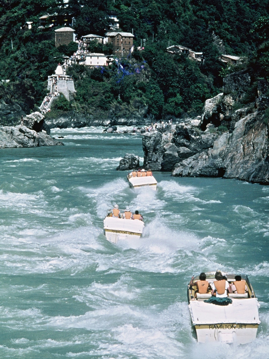 Three jet boats navigate a river.