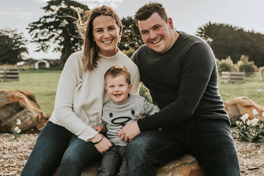 A mum and dad sitting on a rock with their young son.