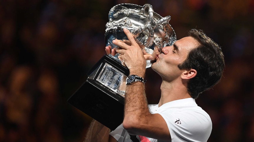 Roger Federer kisses his trophy and displays his sponsored watch