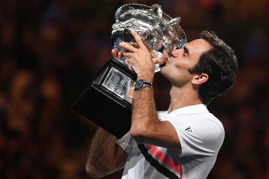 Roger Federer kisses his trophy and displays his sponsored watch