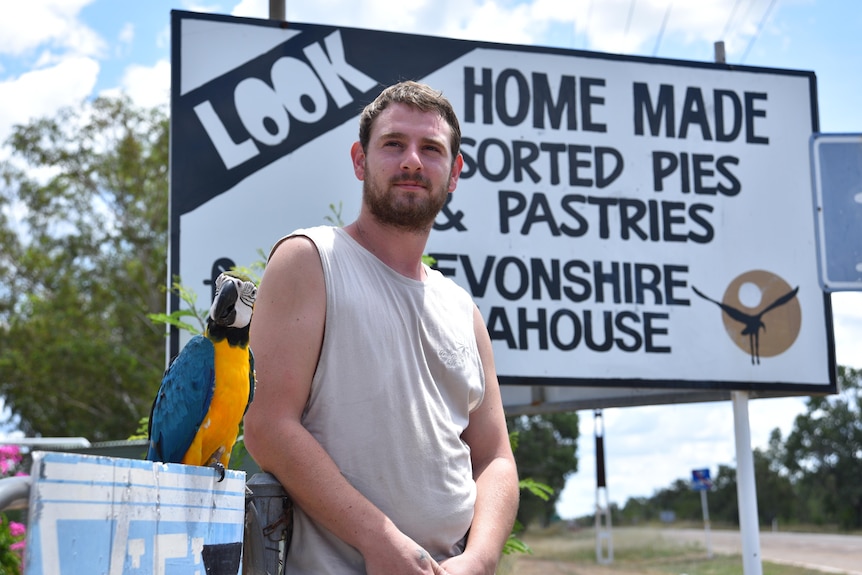 A young man stands in front of a sign with his bird.